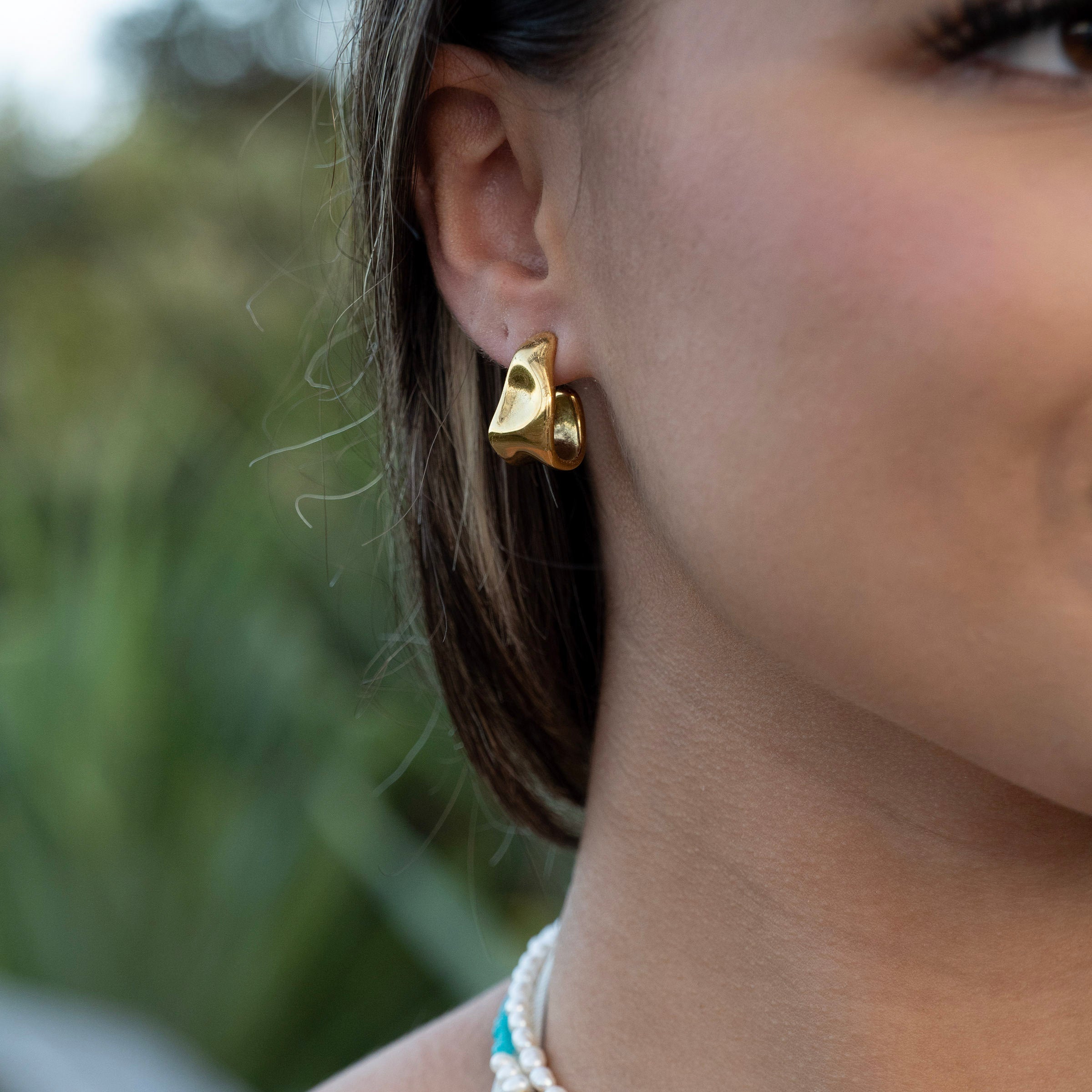 Gold PVD waterproof stud earrings worn on ear, tarnish-free stainless steel organic-shaped earrings for everyday and beach wear