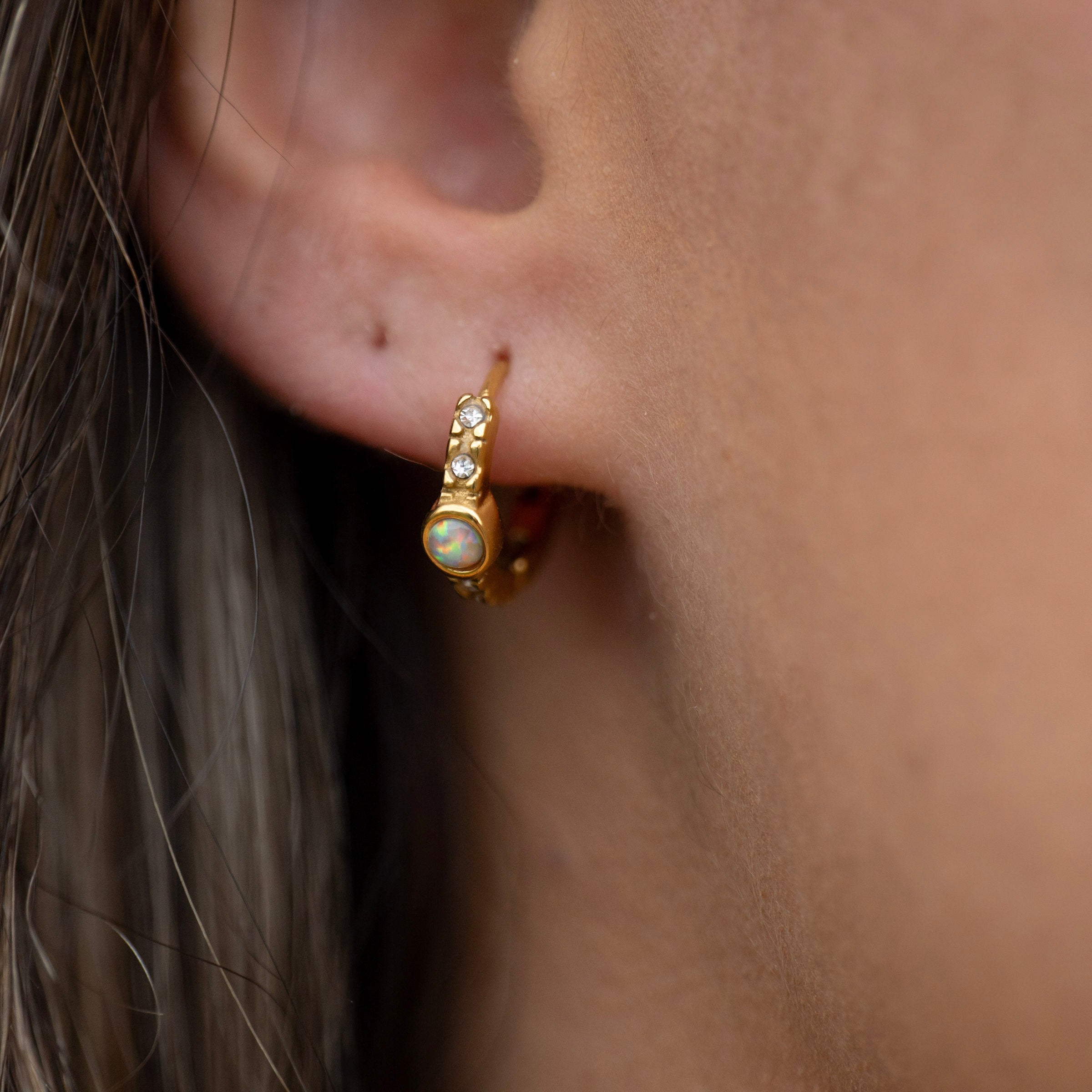 Gold PVD waterproof opal huggie earrings worn on ear, tarnish-free stainless steel huggies with opal and crystal details