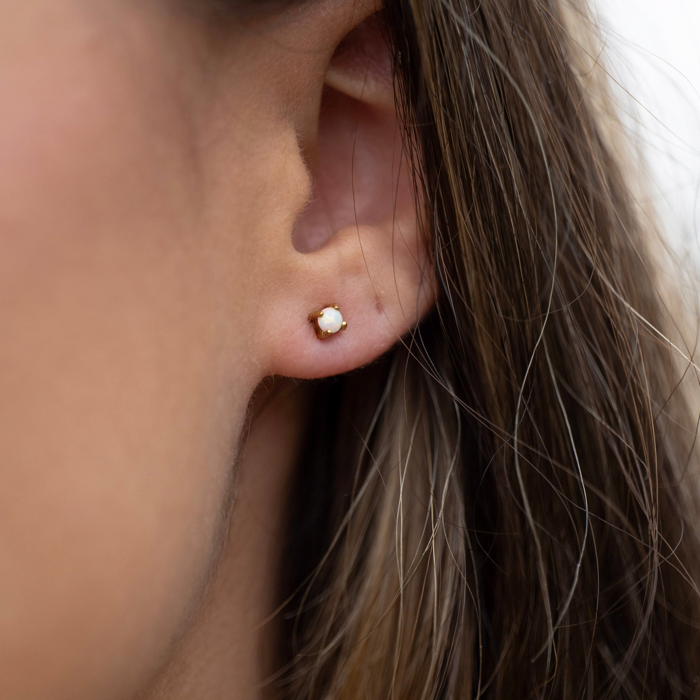 Gold PVD waterproof opal stud earrings worn on ear, tarnish-free stainless steel gemstone studs for everyday and beach wear