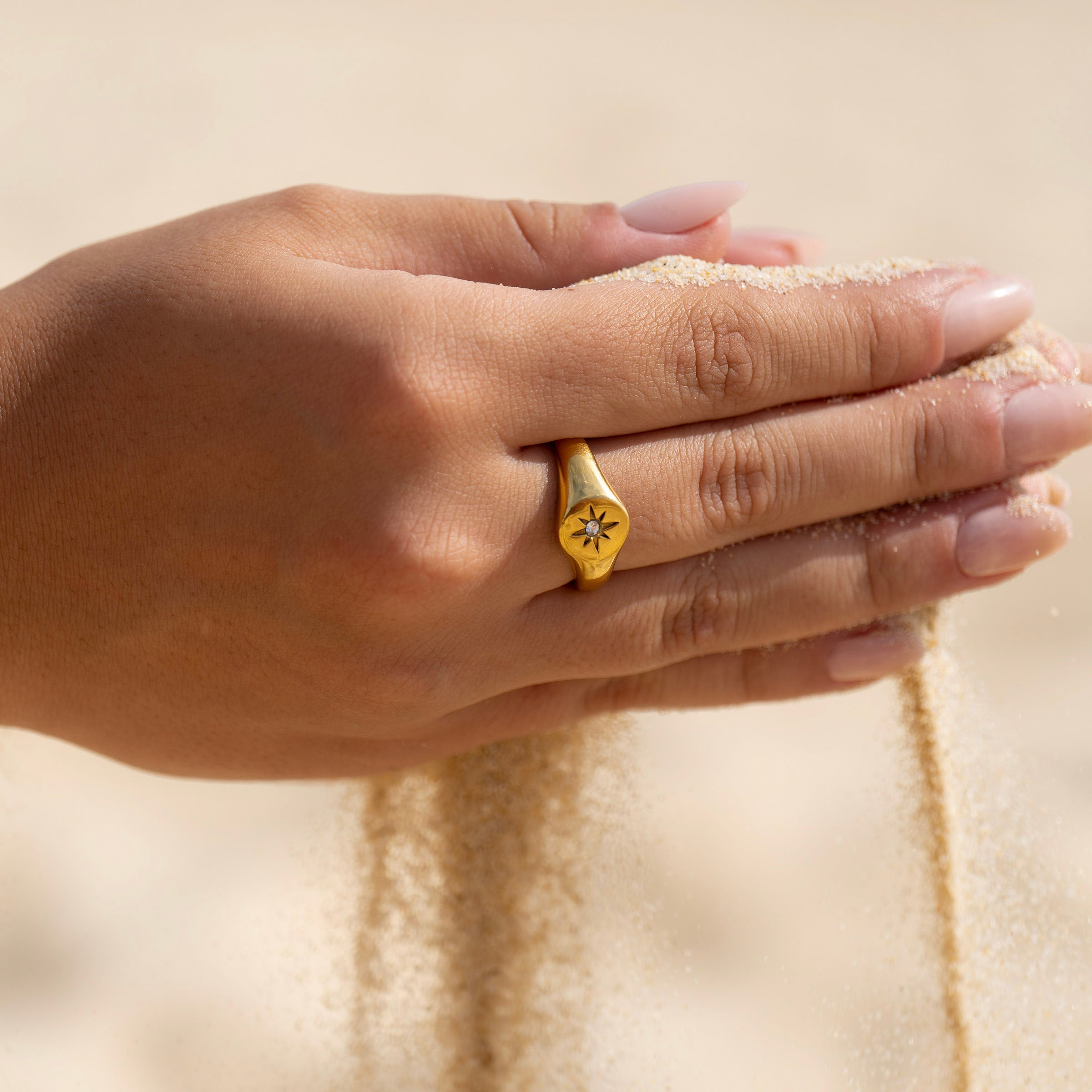 Minimal gold signet ring with star detail, worn on sandy hands, tarnish-free everyday jewellery