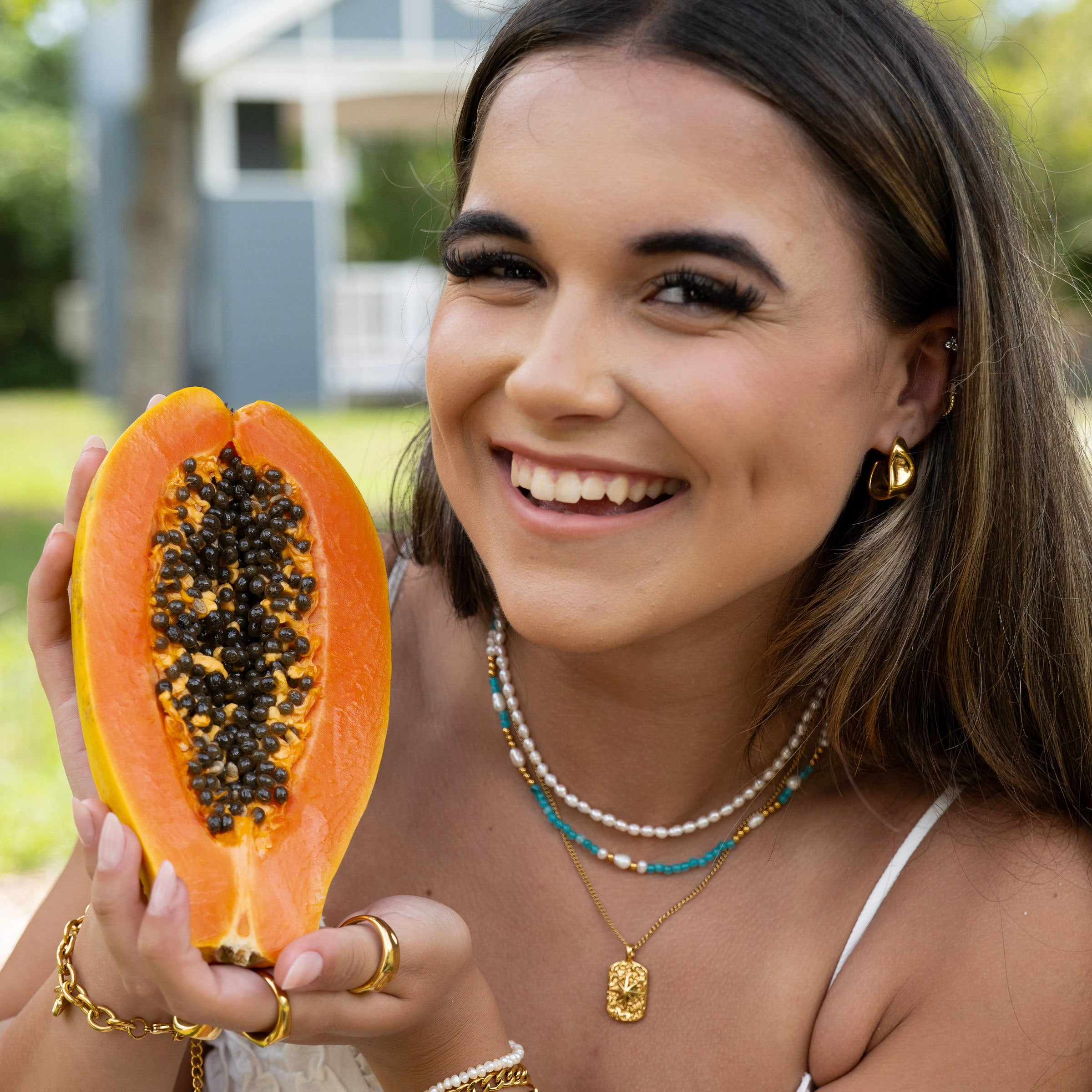 Model wearing a layered gold necklace stack with freshwater pearls, turquoise beads and textured gold pendant outdoors
