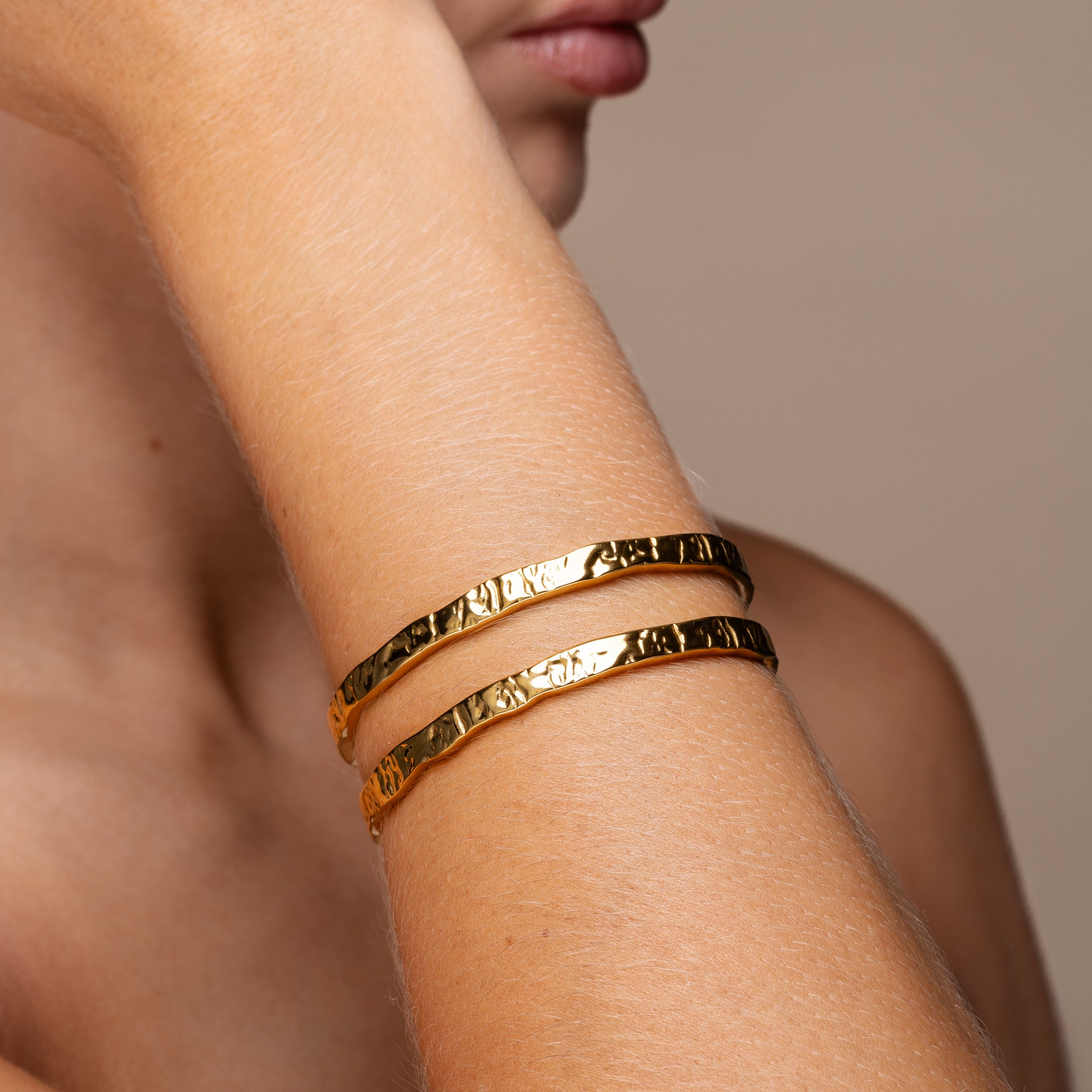Woman wearing the Erosion Cuff Bracelet in 18K PVD gold — textured, waterproof cuff shown on wrist in natural light.