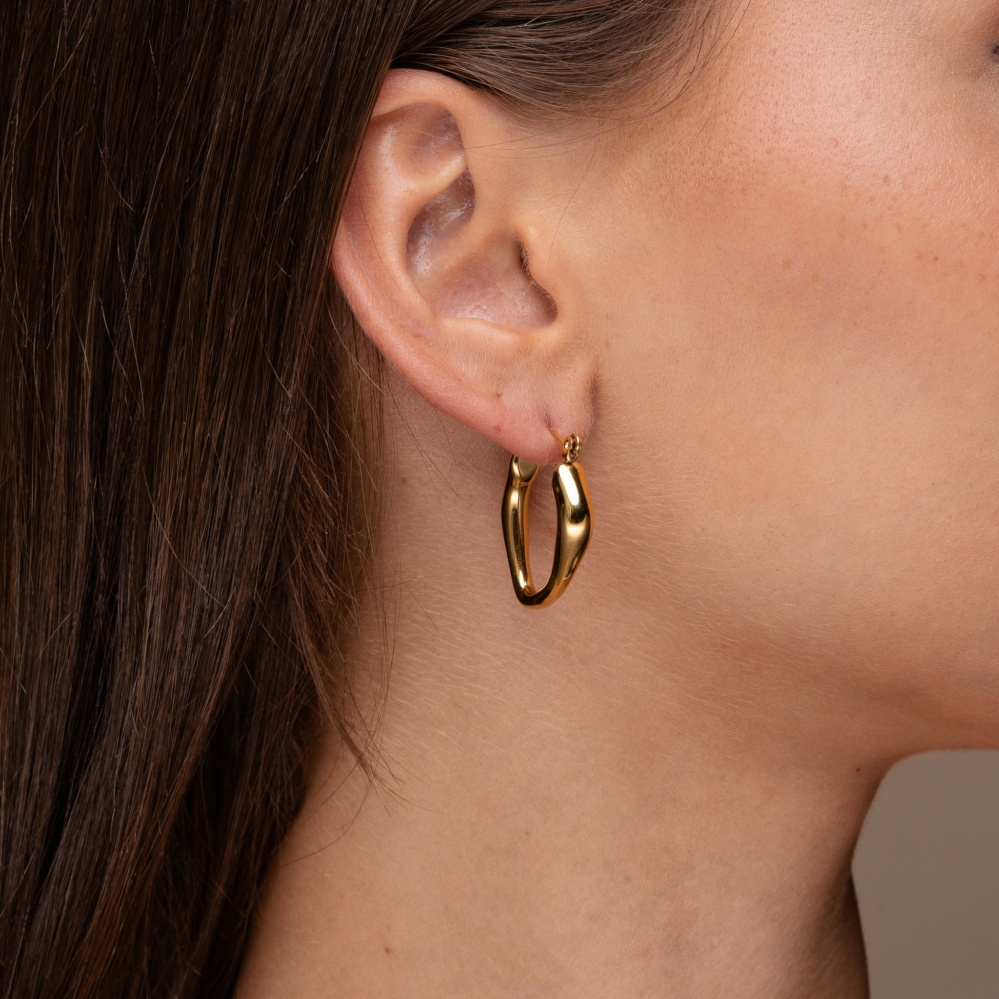 Elara Melt Hoops worn on ear. 18K PVD elongated molten oval hoop, waterproof tarnish free. Maevi jewellery